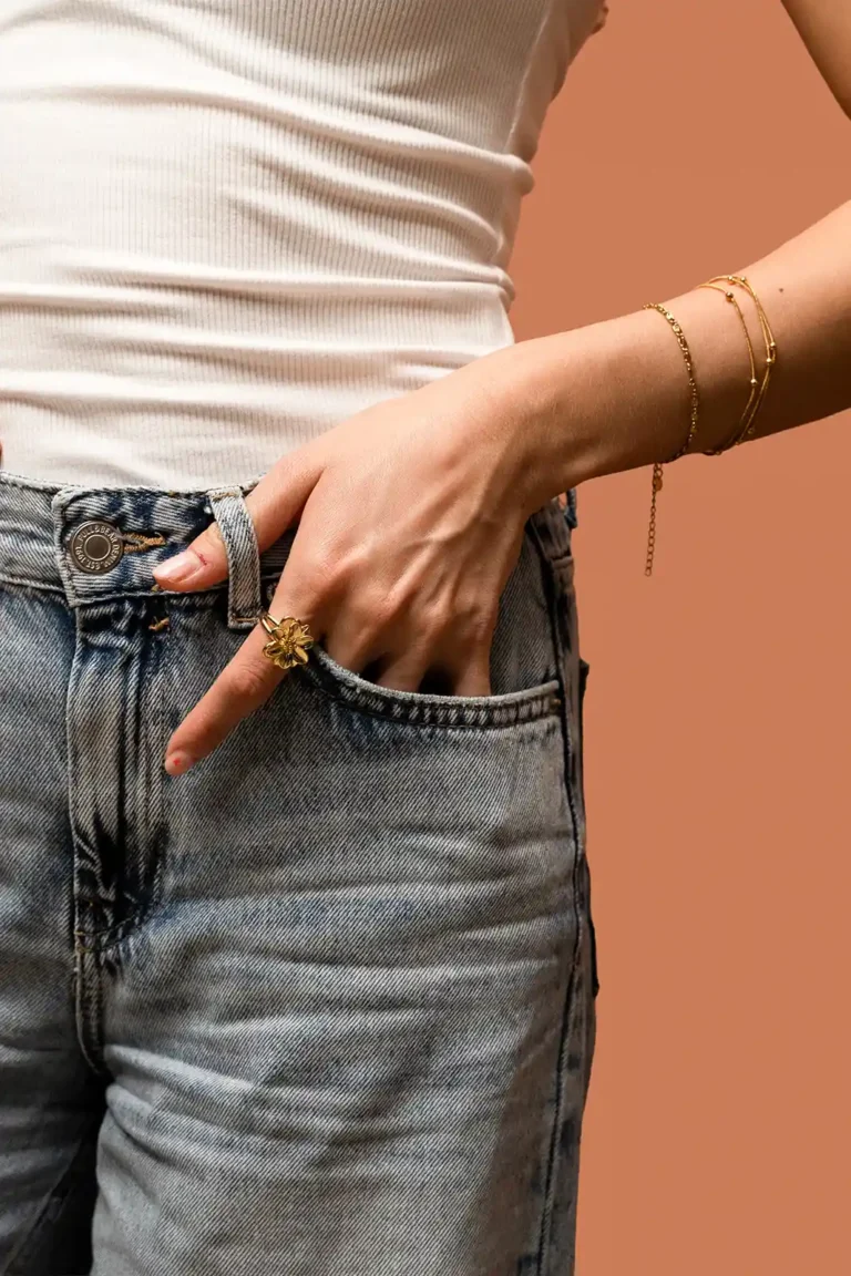 Modelo con jeans luciendo un conjunto de pulseras doradas finas en la muñeca y el anillo Roseta en el dedo índice.